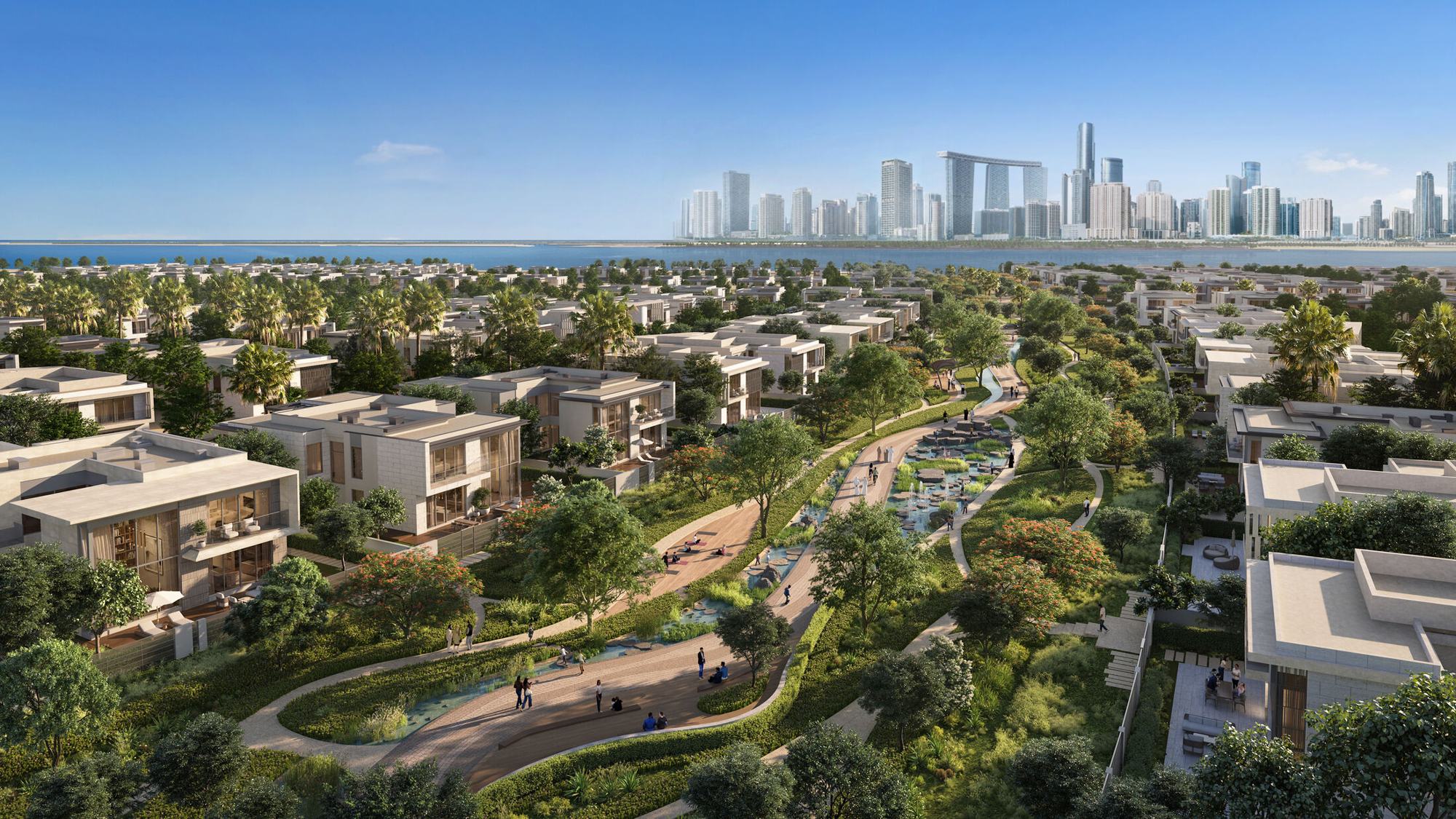 Talay from the air: villas either side of a landscaped green spine and water channel, with the Abu Dhabi skyline across the water